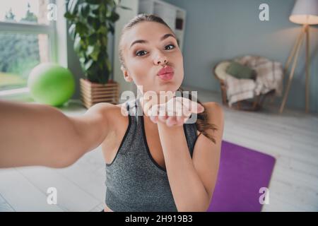 Autoportrait d'une jolie petite fille gaie qui fait du travail physique et vous envoie un baiser d'air dans un studio à la maison léger à l'intérieur Banque D'Images