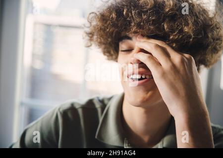 Un adolescent souriant se frottant les yeux à la maison Banque D'Images