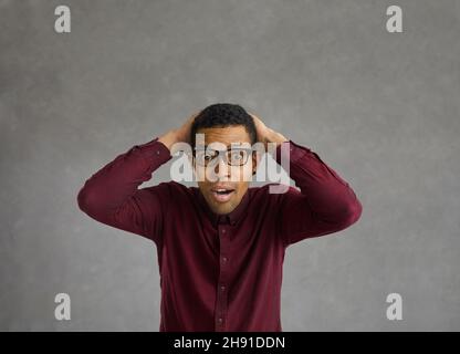 Portrait d'un jeune homme à la peau sombre qui saisit sa tête avec une expression surprise sur son visage. Banque D'Images