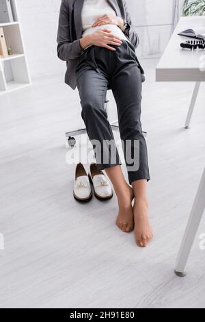 vue partielle de la femme enceinte sans chaussures assise sur une chaise dans le bureau Banque D'Images