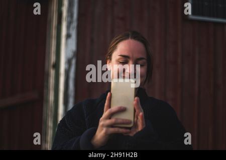 Femme souriante prenant le selfie à travers le smartphone contre le cottage Banque D'Images