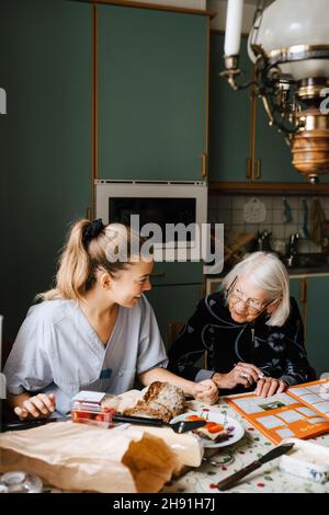 Infirmière souriante enseignant la femme âgée à la table à manger dans la cuisine Banque D'Images