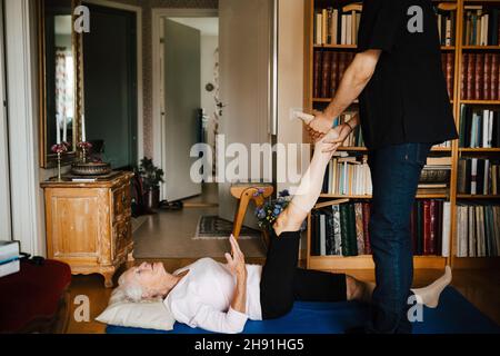 Section médiane du soignant masculin guidant la femme âgée lors de l'exercice à la maison Banque D'Images