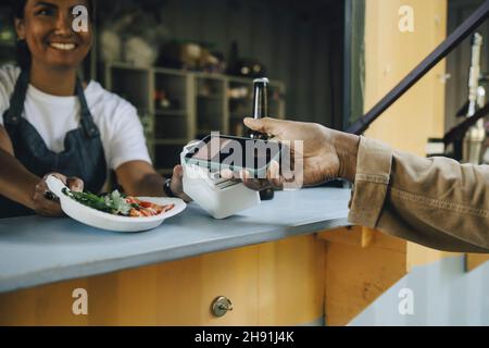 Image rognée du client effectuant un paiement sans contact sur un camion alimentaire Banque D'Images