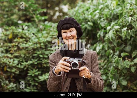 Portrait d'une femme âgée souriante avec caméra contre les plantes dans le parc pendant les vacances Banque D'Images