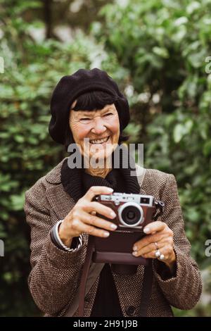 Femme âgée souriante avec caméra dans le parc Banque D'Images