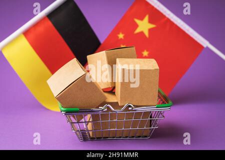 Boîtes en carton dans un panier alimentaire et drapeaux de la Chine et de l'Allemagne sur fond coloré, le concept de commerce entre pays Banque D'Images