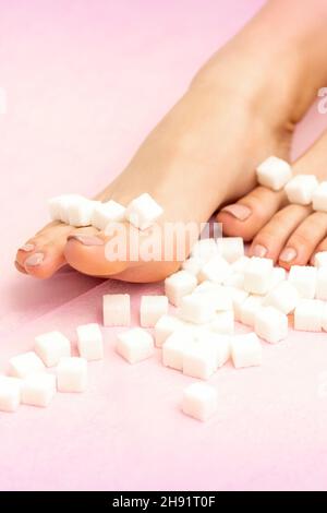 Cubes de sucre couchés sur une rangée de pieds femelles sur fond rose avec espace de copie, concept d'épilation Banque D'Images