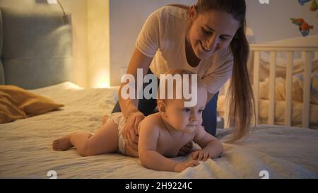 Portrait de mère et de bébé souriants dans des couches couchés sur le lit la nuit Banque D'Images