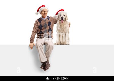 Homme âgé avec un chien Labrador Retriever portant des chapeaux de noël et assis sur un panneau isolé sur fond blanc Banque D'Images