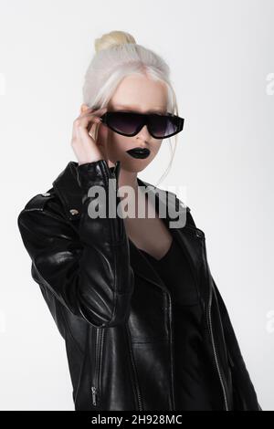 Modèle albino tendance en cuir noir veste tenant des lunettes de soleil isolé sur blanc Banque D'Images