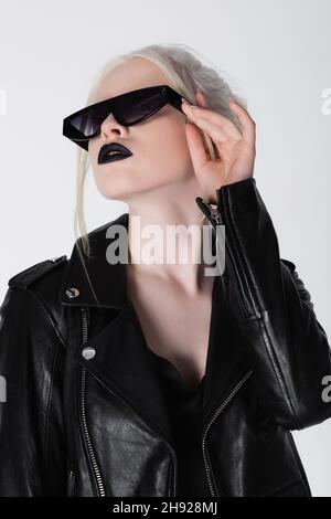 Femme albino tendance en cuir noir veste tenant des lunettes de soleil isolé sur blanc Banque D'Images