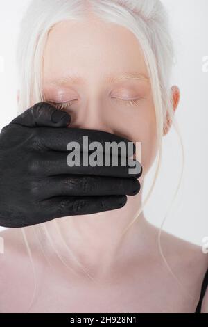 Main mâle dans la peinture noire couvrant la bouche de la femme albino isolée sur blanc Banque D'Images