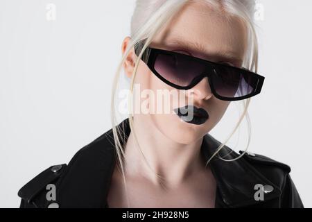 Femme albino tendance en lunettes de soleil et veste en cuir isolée sur blanc Banque D'Images