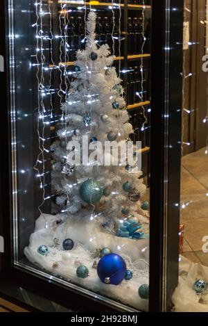 Sapin de Noël blanc derrière le verre.Sapin de Noël artificiel élégant avec boules bleues et bleues.Nouvelle année de la boutique. Banque D'Images