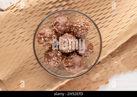 Plusieurs bonbons au chocolat sucré avec noix dans un bol en verre sur papier artisanal, vue rapprochée du dessus. Banque D'Images