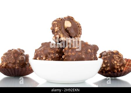 Plusieurs bonbons au chocolat doux avec des noix sur une soucoupe en céramique blanche, gros plan, isolés sur du blanc. Banque D'Images