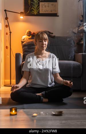 Pratiquer le yoga en position lotus assis sur un tapis dans la salle de séjour le soir.Les mains de mudra posent Banque D'Images