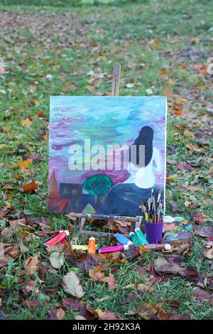 Chevalet avec peintures et peinture avec femme assise sur toile dans le parc d'automne. Banque D'Images