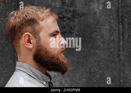Un portrait de profil d'un jeune homme beau avec une coiffure tendance sur fond gris.Toilettage et barbershop commercial adv concept copie fre Banque D'Images