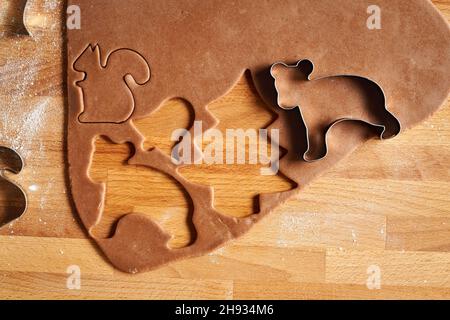 En coupant les formes d'animaux et d'arbres de la pâte à pâte déployée pour préparer des biscuits de Noël faits maison au pain d'épice Banque D'Images