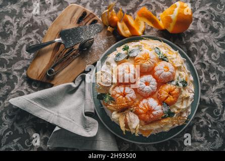 Gâteau Pavlova basse lumière décoré de mandarines fraîches, de physalis à la menthe caramel et versé avec le dessert à base de meringue au sucre en poudre nommé d'après les Russ Banque D'Images