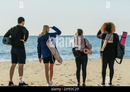 Dos de quatre personnes debout face à la mer tout en portant des tapis de yoga Banque D'Images