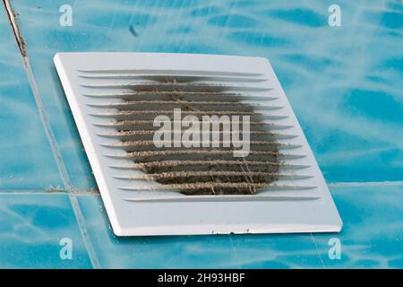 Ventilateur de la salle de bains très sale. Ventilateur très sale avec grille en plastique blanc. L'équipement électrique doit être nettoyé. Carrelage bleu avec motif dans la salle de bains Banque D'Images