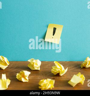 Boules de papier froissés et bloc-notes avec point d'exclamation sur bureau en bois. Fond de mur bleu.Réflexion, solution, entreprise, concept d'idée Banque D'Images