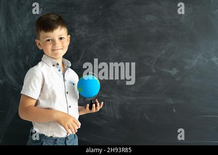 élève de l'école élémentaire debout avec un globe près d'un tableau de craie dans une salle de classe avec un tableau noir en arrière-plan.Leçon de géographie pour Banque D'Images