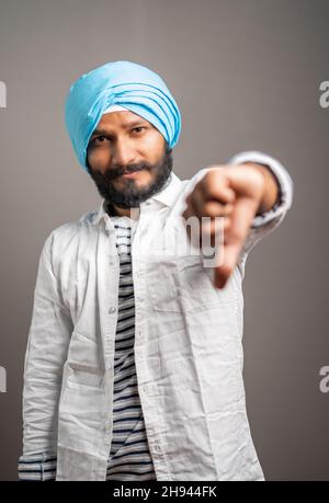 Photo portrait d'un Indien sikh dépeint en montrant le pouce vers le bas ou le geste déplaît en regardant l'appareil photo - concept de mauvais support ou de notation de client Banque D'Images