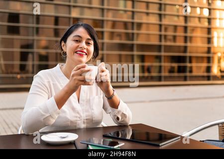 femme d'affaires souriant avec une tasse de café dans ses mains sur la terrasse d'un café-restaurant, concept d'entrepreneur numérique et de style de vie urbain, copy spa Banque D'Images