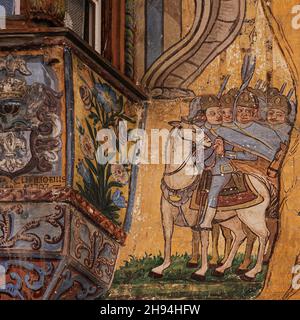 Détail carré de l'art peint du XVIIe ou XVIIIe siècle sur la façade colorée de la Haus Claglüna, une demeure familiale traditionnelle historique dans le canton d'Ardez, des Grisons ou des Grisons, dans l'est de la Suisse.Une troupe de cavalerie à côté d'une fenêtre d'oriel richement décorée se cache derrière un arbre d'un autre groupe de cavaliers, peut-être pour les embuer.La propriété est mieux connue sous le nom de "la maison Adam et Eve" d'une plus grande œuvre d'art, datant de 1647, représentant le jardin d'Eden. Banque D'Images