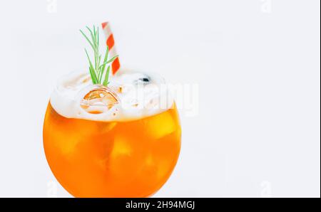 Gros plan verre de glace cocktail Aperol Spritz décoré de paille rouge et de romarin servi dans un verre de vin sur fond blanc. Banque D'Images