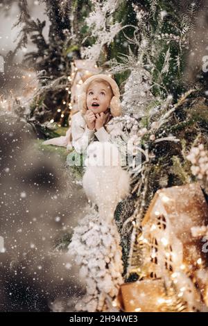 photo de la petite fille se demande dans des vêtements légers se trouve sur une décoration de noël avec des arbres et un petit hibou blanc Banque D'Images
