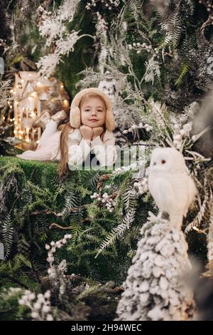 image de petite fille attrayante en vêtements légers se trouve sur une décoration de noël avec des arbres et un petit hibou blanc Banque D'Images