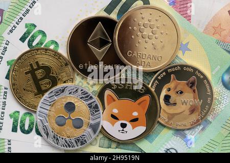 Bitcoin, Cardano, Shiba Inu, Ethereum, Ripple,Et Dogecoin pièces physiques qui s'élève sur des billets de 100 et 10 euros. Banque D'Images