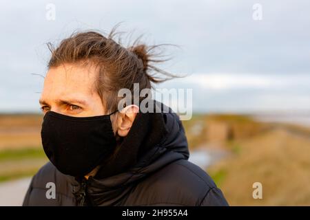 Un jeune homme portant un masque noir lavable pendant la pandémie du virus corona Covid-19 Banque D'Images