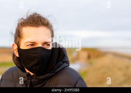 Un jeune homme portant un masque noir lavable pendant la pandémie du virus corona Covid-19 Banque D'Images