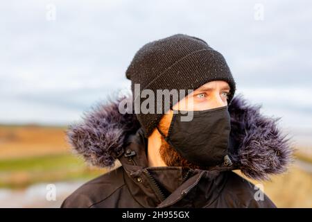Un jeune homme portant un masque noir lavable pendant la pandémie du virus corona Covid-19 Banque D'Images