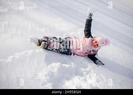 L'enfant joue avec la neige.La petite fille aime marcher dans la nature, s'amuser et faire du toboggan sans traîneau le jour d'hiver ensoleillé Banque D'Images