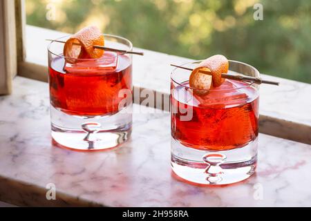 Negroni cocktail amer avec Orange Twist over Ice in Rocks Glass dans le rebord de la fenêtre en marbre Banque D'Images