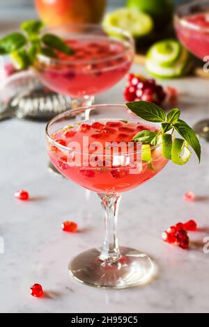 Des cocktails de basil Martini à la grenade avec des verres en forme de coupé et de citron vert sur un comptoir en marbre Banque D'Images