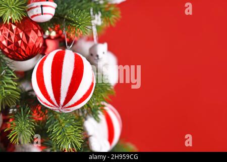 Boule décorative de Noël à rayures suspendue à la branche de l'arbre devant un fond rouge avec espace pour les copies Banque D'Images