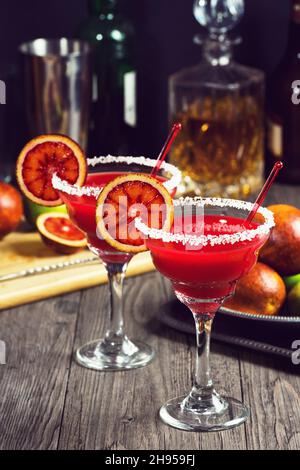 Margaritas d'orange de sang servies dans un verre à tiges avec une bordure salée et des ingrédients en arrière-plan Banque D'Images