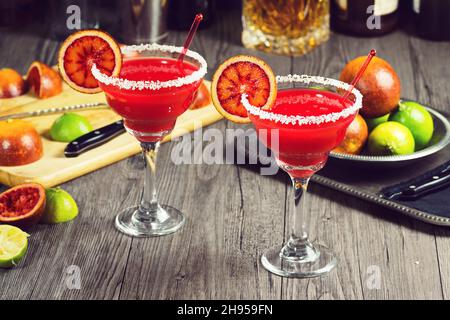 Margaritas d'orange de sang servies dans un verre à tiges avec une bordure salée et des ingrédients en arrière-plan Banque D'Images