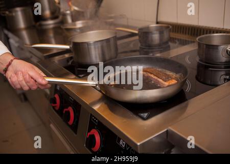 Gros plan sur la cuisinière du chef du restaurant qui friture le saumon Banque D'Images