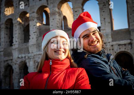 Vacances de Noël.Un jeune couple charmant prenant une photo devant le Colisée en chapeaux rouges du Père Noël.Sentiment de bonheur et d'amour. Banque D'Images