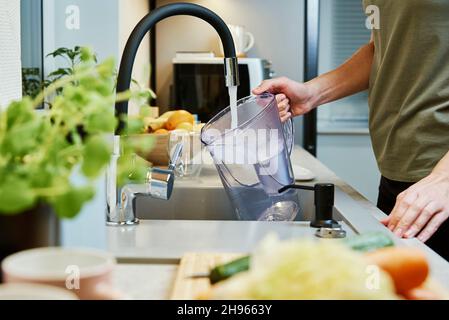 Femme versant de l'eau du robinet dans la verseuse d'eau à la cuisine Banque D'Images