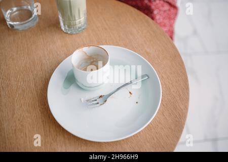 Utilisé une tasse de café vide avec une assiette blanche sale et une fourchette sur une table en bois dans un café après avoir bu Banque D'Images